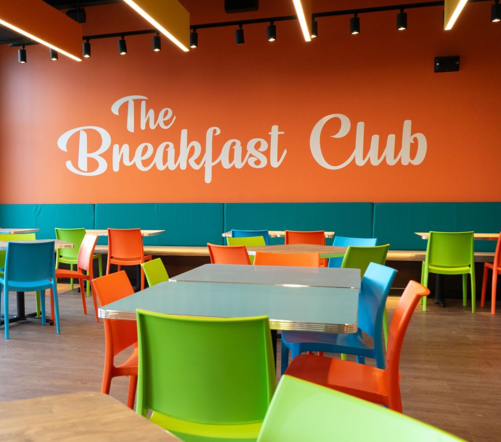 seating area for the breakfast club with colorful chairs and logo on wall